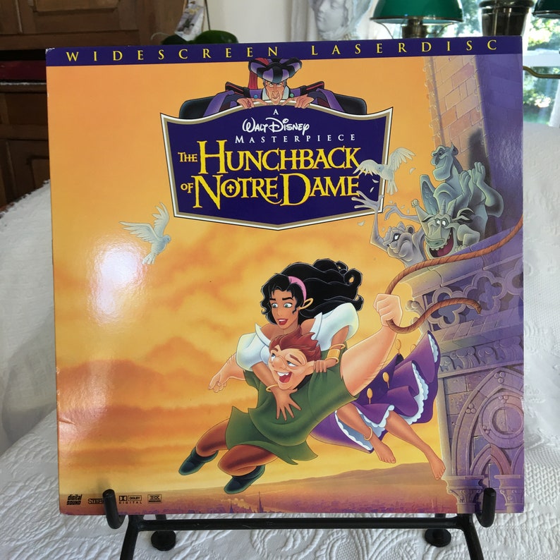 May include: A Walt Disney Masterpiece laserdisc featuring the animated film The Hunchback of Notre Dame. The cover art features Esmeralda and Phoebus flying through the air, with a gargoyle in the background. The title is written in a gold font with a red and blue border.