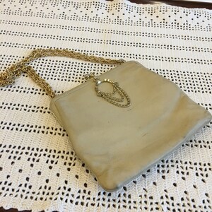 Könnte beinhalten: Eine beige Leder-Clutch mit einem goldenen Kettenriemen und einem dekorativen goldenen Verschluss.