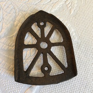 May include: A cast iron trivet with a circular design. The trivet has a decorative, openwork pattern with a central circle and radiating spokes.