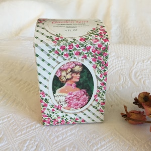 May include: A white box with green and white stripes and pink flowers. The box has a label that says "Garden Girl Charisma Cologne" and "4 fl. oz.". The box features a picture of a woman with blonde hair wearing a white dress and holding a bouquet of pink flowers.
