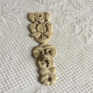 May include: A white cast iron decorative wall hook with a floral design and a face at the bottom.