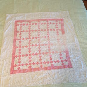 Pode incluir: Uma colcha branca com um padrão de diamantes rosa. A colcha tem um fundo branco com pequenos pontos rosa e um padrão de diamantes rosa maiores.