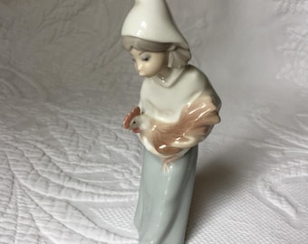 Estatueta de porcelana Lladro vintage de menina carregando um galo. Vestindo uma saia azul e top e chapéu brancos.