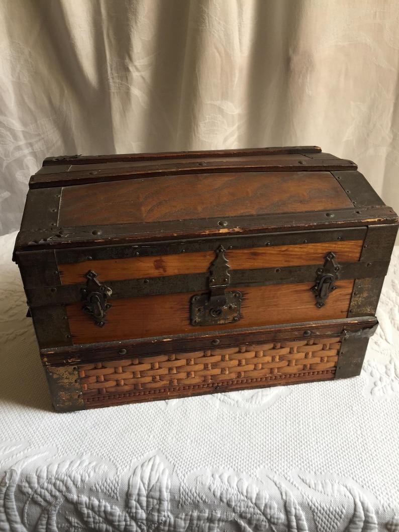 Puede incluir: Un cofre de madera vintage con un fondo de mimbre tejido. El cofre tiene detalles met&aacute;licos y una cerradura.