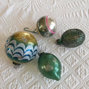 Pode incluir: Quatro enfeites de Natal vintage. Um é um enfeite verde em forma de gota. Outro é uma bola verde e prateada com uma faixa rosa. Um terceiro é um enfeite oval verde e canelado. O último é um enfeite de bola azul, prateado e dourado.