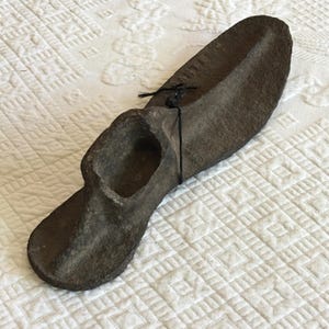 May include: A gray cast iron shoe last, a tool used by shoemakers to shape shoes. The last is tied with a black string.
