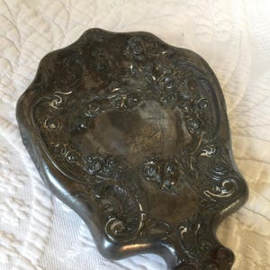 May include: A silver-toned hand mirror with an ornate, floral design. The mirror is shaped like a scallop shell and has a handle.