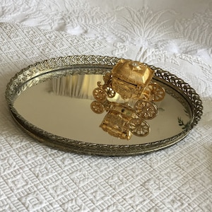 Vintage gouden ovale spiegelbak met opengewerkte bloemen en bladeren ontwerpen. Kartonnen achterkant met 4 rubberen voetjes.