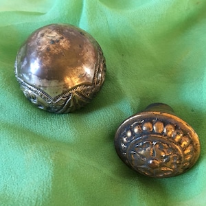 Könnte beinhalten: Zwei antike Türknauf aus Messing mit aufwendigen Designs. Der größere Knauf hat eine abgerundete Form mit einem Blumenmuster, während der kleinere Knauf eine kreisförmige Form mit einem erhabenen Blumenmuster hat.