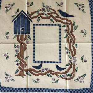 May include: A cream-colored fabric with a blue and brown stencil design. The design features a birdhouse, birds, branches, and berries. The fabric has a blue and white checkered border and the text "PILLOW COVER" at the bottom.