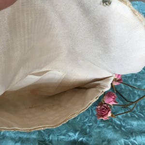 May include: The inside of a white fabric clutch purse with a small pocket. The purse is made of a woven material and has a smooth lining. The purse is open and the lining is visible.
