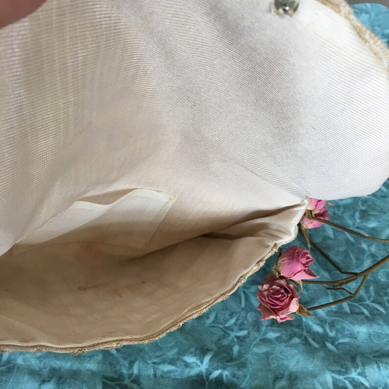 May include: The inside of a white fabric clutch purse with a small pocket. The purse is made of a woven material and has a smooth lining. The purse is open and the lining is visible.