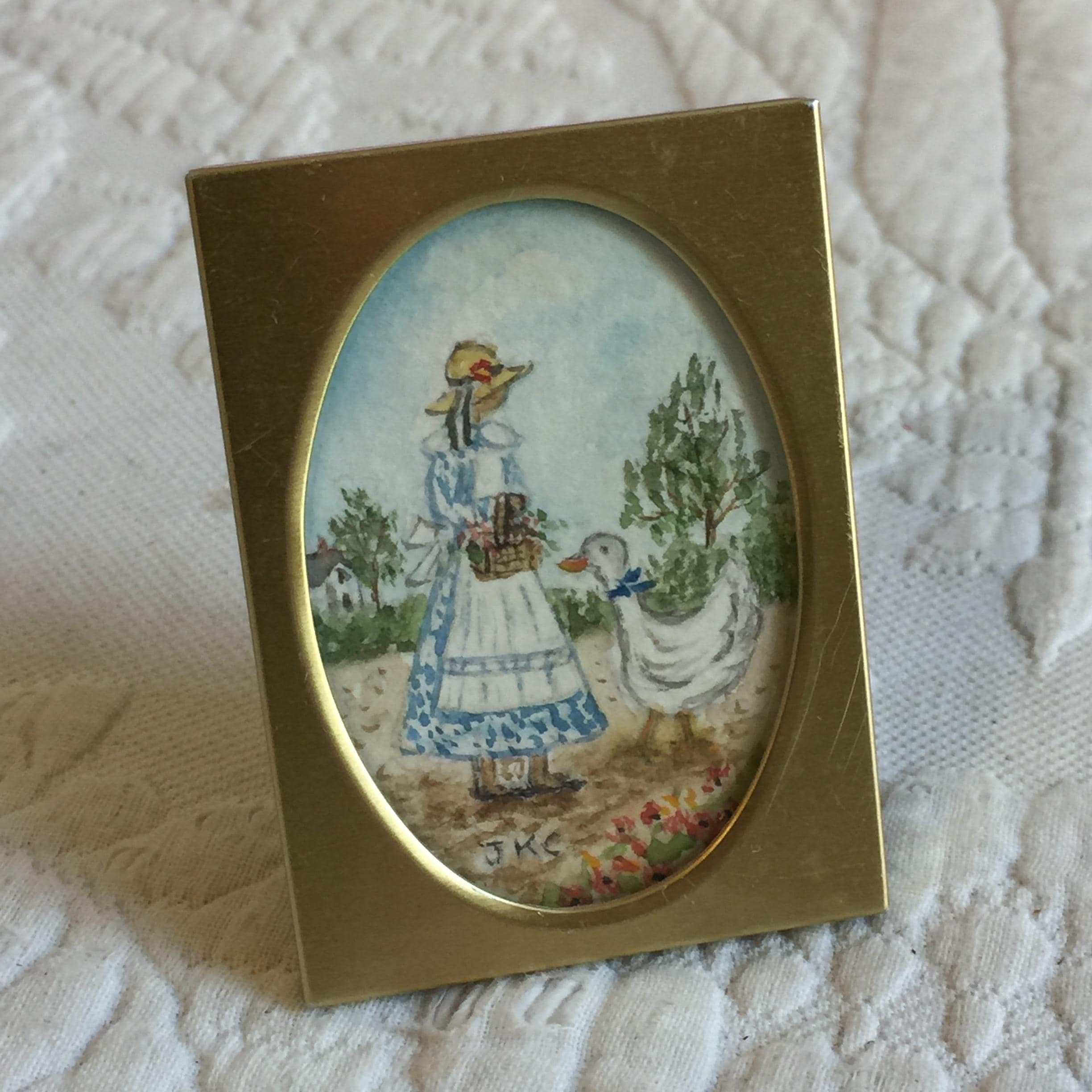 Cornice in ottone in miniatura vintage con acquerello ovale di JKC. Ragazza che trasporta un cesto di fronte alla sua oca. Miniatura originale in acquerello.