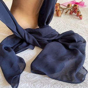 May include: A navy blue sheer scarf tied in a knot around a mannequin's neck. The scarf is made of a lightweight, flowing fabric.