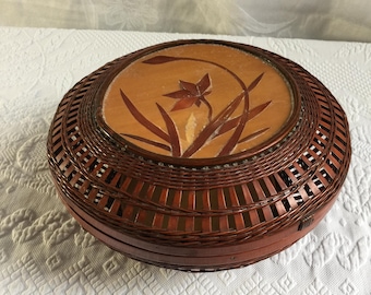 ヴィンテージ風のオープンウィーブ中国式バスケット容器（蓋付き）。上部には装飾的な花柄の木製デザインが施されています。