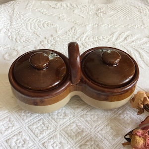 以下が含まれることがあります： ふた付きのハンドルが付いた茶色とベージュのセラミック製の二重皿。調味料や軽食を盛り付けるのに最適です。