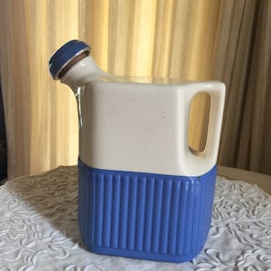 May include: A white ceramic jug with a blue lid and a blue stripe around the bottom. The jug has a handle and a spout.
