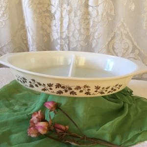 May include: A white divided casserole dish with a brown floral pattern. The dish has two sections and is oval shaped.