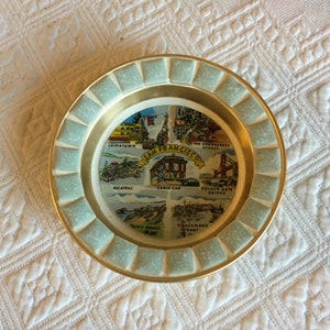 May include: A round, gold-rimmed plate with a mosaic design. The plate features a colorful illustration of San Francisco landmarks, including Chinatown, Alcatraz, the Golden Gate Bridge, Fisherman's Wharf, and a cable car.