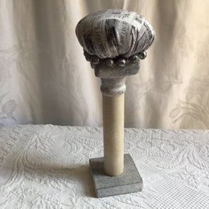 Handmade Hat Stand, Wood Pillar. Newsprint Type Fabric Hat Cushion on the Gray and Beige Wood Pillar. Large Bead Trim and Long Black Tassel.