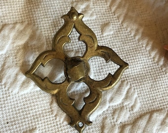 May include: A gold-toned metal decorative piece with a four-pointed star design and intricate cutouts. The piece has a small hole at the bottom.