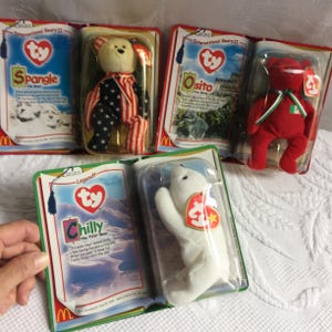 May include: A collection of Ty Beanie Babies in their original packaging. The collection includes a polar bear named Chilly, a bear with an American flag design, and other bears. The packaging features the Ty heart logo and the McDonald's logo.