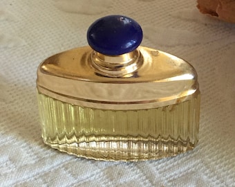 Puede incluir: Un frasco de perfume vintage con tapa dorada y tapón de vidrio azul. El frasco es transparente y tiene una superficie texturizada.