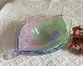 May include: A clear glass bowl with a handle. The bowl is decorated with swirls of pink, green, and blue.