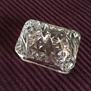Könnte beinhalten: Eine klare Glasringbox mit einem diamantförmigen Design. Die Box hat eine strukturierte Oberfläche mit einem Sternmuster.