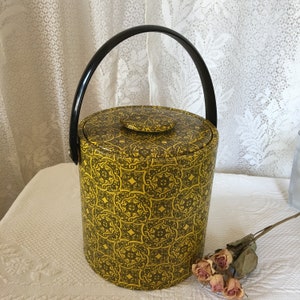 Könnte beinhalten: Ein gelber und schwarzer Eiseimer mit geometrischem Muster. Der Eimer hat einen schwarzen Griff und einen Deckel.