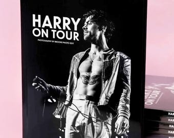 Op de afbeelding: Een zwart-wit fotoboek met harde kaft getiteld HARRY ON TOUR PHOTOGRAPHY BY BROOKE PHOTO EDIT. De omslag toont een monochrome afbeelding van een persoon met een vlindertattoo op de borst, gekleed in een jasje en een broek.