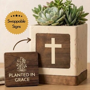 May include: A square, off-white planter with a wooden cross design and a variety of succulents. A smaller wooden sign with the text "PLANTED IN GRACE" is next to the planter. The sign is swappable.