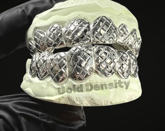 Puede incluir: Grillz plateados con un patrón de corte de diamante, exhibidos en un molde dental verde claro. El texto "Gold Density" es visible. El fondo es negro.