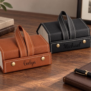 May include: Two rectangular, foldable storage cases with carrying handles and snap closures. One case is tan with the name Evelyn embossed on the front, and the other is black with the name Michael embossed on the front. Both feature white stitching.