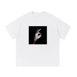 Pode incluir: Camiseta branca com um gráfico quadrado de uma mão fazendo o gesto 'ok'. A mão usa uma luva prateada brilhante em um fundo preto. A camiseta tem mangas curtas e gola redonda.