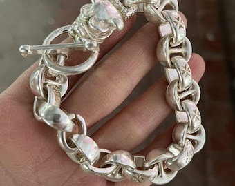 May include: A silver bracelet featuring a toggle clasp and a series of large, rounded links. Each link is adorned with a starburst design. The clasp has a detailed, ornate design.