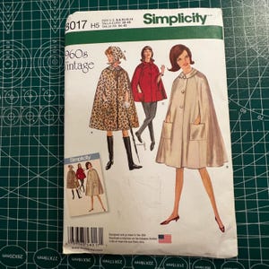 May include: A Simplicity sewing pattern envelope, number 8017, featuring illustrations of three capes. The pattern includes sizes 6, 8, 10, 12, and 14. The designs show a leopard print cape with a hood, a solid red cape, and a solid light-colored cape.