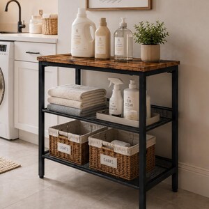 May include: A three-tier laundry storage cart with a dark wood-grain top and black metal frame. The top shelf holds laundry detergent bottles and a small potted plant. The middle shelf holds folded towels and cleaning supplies. Two woven baskets labeled LIGHTS and DARKS sit on the bottom shelf.