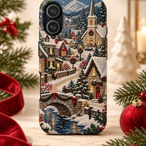 May include: A smartphone case featuring a detailed winter village scene with snow-covered houses, a stone bridge over a stream, evergreen trees, and a church steeple. The design includes festive red wreaths and ribbons against a snowy landscape.