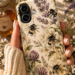 Puede incluir: Funda de teléfono de color crema con un diseño de acuarela de abejas, lavanda y flores. La funda tiene un acabado mate y un diseño protector. La funda está diseñada para un teléfono inteligente con cámara de doble lente.