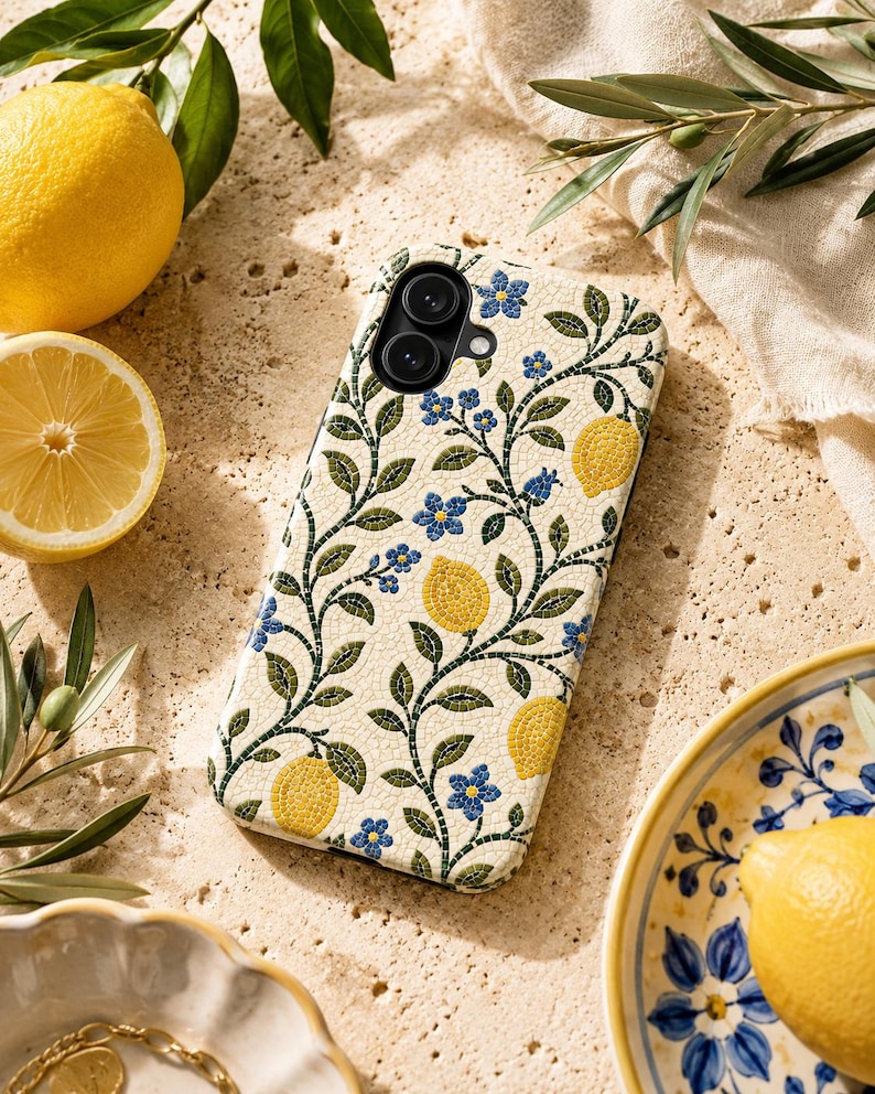 Pode incluir: Uma capa de telefone com fundo creme com um padr&atilde;o repetido de lim&otilde;es amarelos, flores azuis e vinhas verdes. A capa tem um recorte para uma c&acirc;mera de lente dupla. A imagem tamb&eacute;m inclui lim&otilde;es, folhas e um prato decorativo.