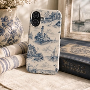 May include: A phone case featuring a blue and cream toile de jouy pattern with illustrations of a lighthouse, sailboats, coastal houses, and a bird. The design includes a small sign that reads TO BEACH, capturing a nautical scene on the back cover.