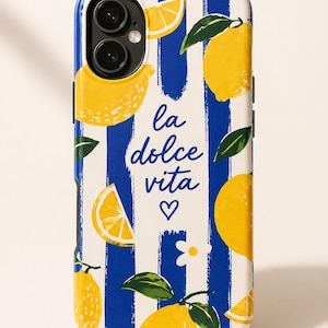May include: A smartphone case featuring a pattern of yellow lemons, green leaves, and small white flowers over vertical navy blue and white stripes. The text "la dolce vita" is printed in blue script in the center, accompanied by a small heart.