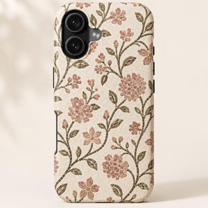 May include: A phone case with a floral mosaic design. The case features a cream-colored background with a pattern of pink flowers and green leaves. The flowers are arranged in a repeating pattern across the surface of the case.