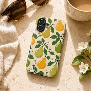 May include: A smartphone case featuring a pear design in yellow and green on a cream backdrop. The case is positioned near sunglasses, a coffee cup, and a white towel. The case has a dual-lens camera.