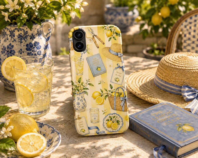 May include: A smartphone case featuring a yellow and white vertical striped pattern decorated with illustrations of lemons, a straw hat, a blue book titled The Lemon Grove Club, a woven basket, a candle, garden shears, and floral arrangements.