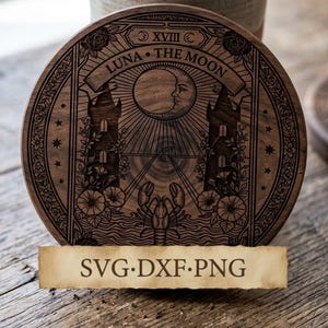 May include: A circular dark wood coaster featuring a laser-engraved tarot card design titled LUNA THE MOON. The artwork depicts a crescent moon, two towers, a lobster, and floral motifs. A rectangular parchment-colored label displays SVG·DXF·PNG.
