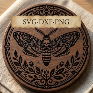 May include: A circular wooden coaster featuring a laser-engraved design of a moth with a skull pattern on its thorax, surrounded by ornate filigree and leaf motifs. A rectangular banner across the center displays the text SVG·DXF·PNG.