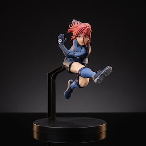 May include: A figurine of a footballer in a dynamic pose, mid-kick. The figure wears a blue uniform with black accents and has red hair. The figurine is mounted on a black stand, set against a dark background.