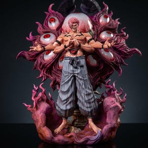 May include: A detailed figurine of a muscular character with multiple arms and a demonic appearance. The figure has a red and purple color scheme, with a large, eye-filled backdrop. The character wears striped pants and stands on a fiery base.